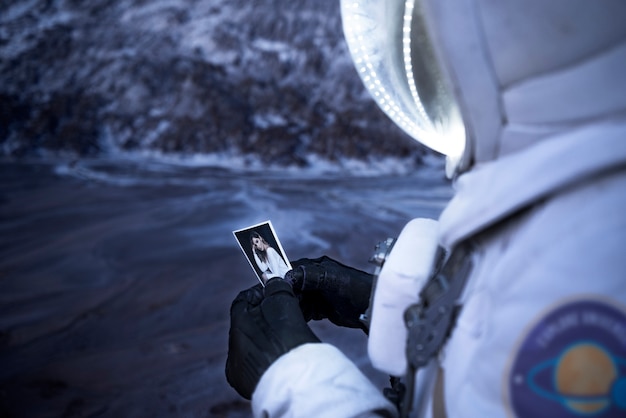 Männlicher astronaut, der ein foto einer frau während einer weltraummission auf einem unbekannten planeten betrachtet