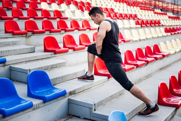Männlicher Athlet, der sein Bein auf Treppenhaus nahe Zuschauertribünen ausdehnt