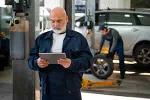 Kostenloses Foto männlicher automechaniker mit tablet-gerät in der autowerkstatt