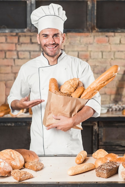 Männlicher Bäcker, der eine braune Papiertüte mit frisch gebackenem köstlichem Brot hält