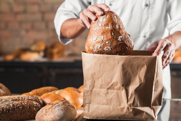 Männlicher Bäcker, der gebackenes Brot in braune Papiertüte setzt