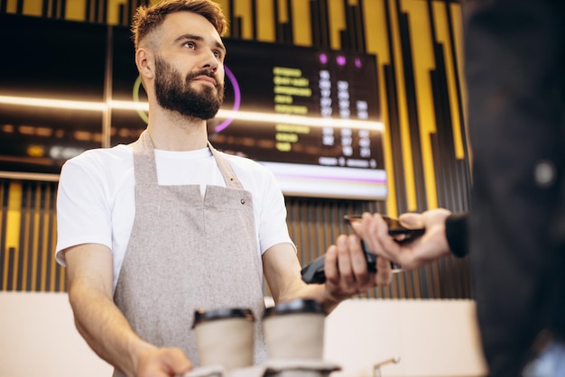 Kostenloses Foto männlicher barista, der ein terminal hält, während der kunde mit karte bezahlt