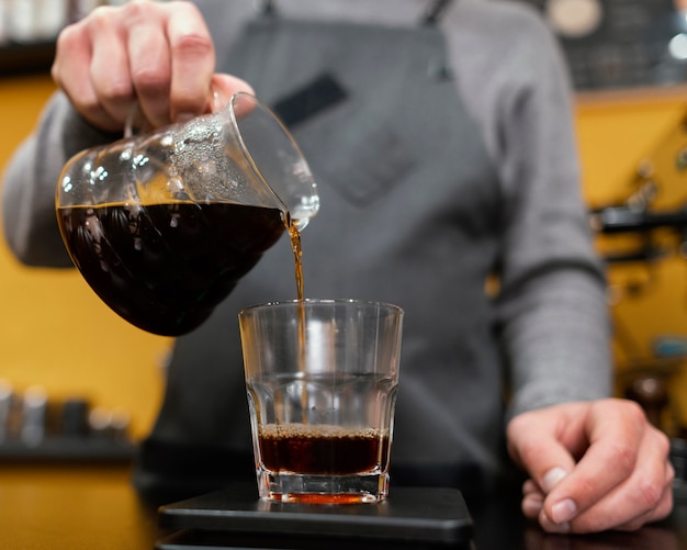 Männlicher Barista, der Kaffee in transparentem Glas gießt