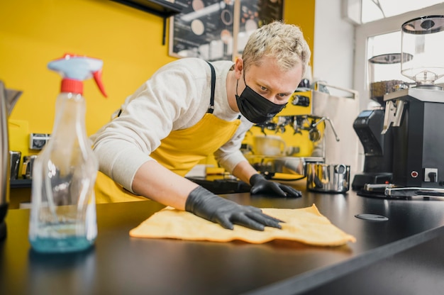 Männlicher Barista mit medizinischer Maskenreinigungstabelle