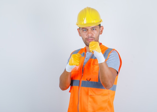 Männlicher Baumeister, der Fäuste als Boxer in der Vorderansicht der Uniform, des Helms, der Handschuhe zeigt.