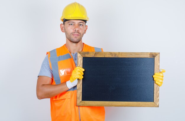 Männlicher Baumeister, der Tafel in Uniform, Helm, Handschuhe, Vorderansicht hält.