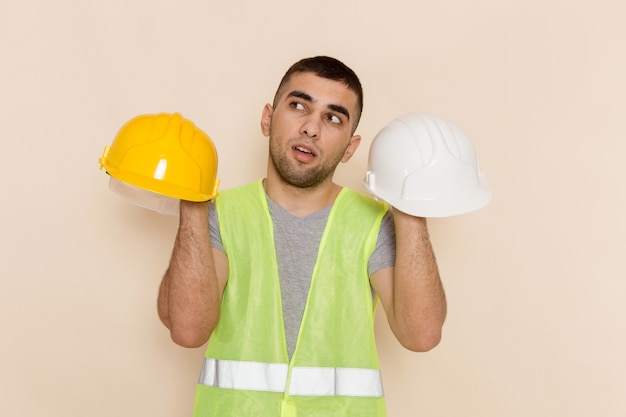 Männlicher Baumeister der Vorderansicht, der Helme hält, die auf hellem Hintergrund denken