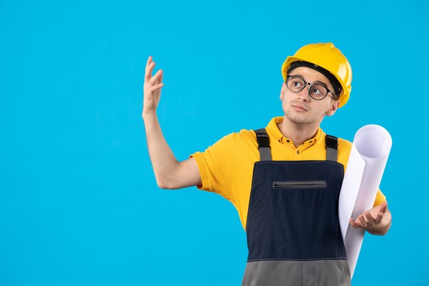 Männlicher Baumeister der Vorderansicht in der Uniform mit Papierplan auf Blau