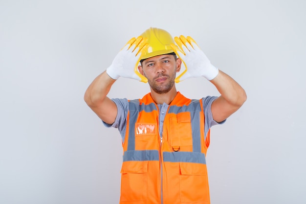 Männlicher Baumeister in Uniform, Helm, Handschuhe, die Fingerrahmen gestikulieren, Vorderansicht.