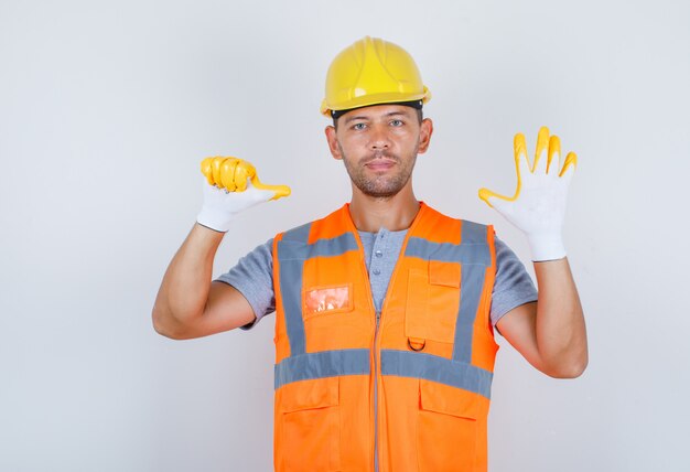Männlicher Baumeister in Uniform, Helm, Handschuhe mit der Nummer sechs mit den Fingern, Vorderansicht.