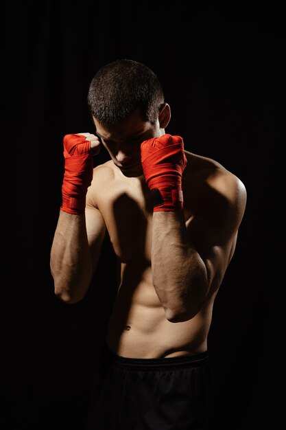 Männlicher Boxer-Kämpfer, der in der selbstbewussten defensiven Haltung mit den Händen in den Verbänden oben aufwirft