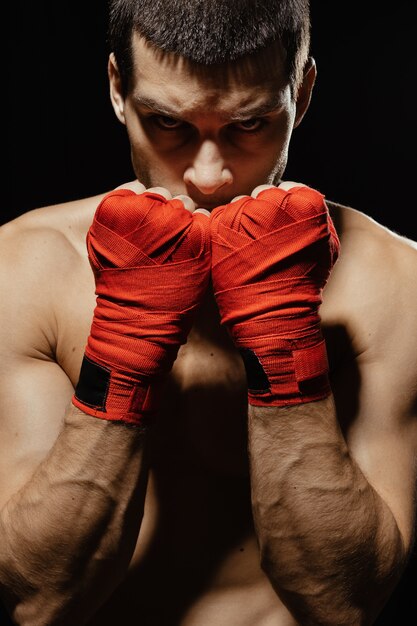 Männlicher Boxer-Kämpfer, der in der selbstbewussten defensiven Haltung mit den Händen in den Verbänden oben aufwirft