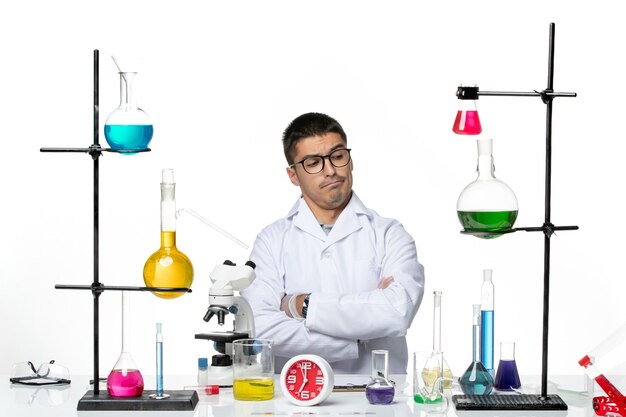 Männlicher Chemiker in der Vorderansicht im weißen medizinischen Anzug, der sitzt und sich auf die Arbeit am kovidpandemischen Labor der weißen Hintergrundviruswissenschaft vorbereitet