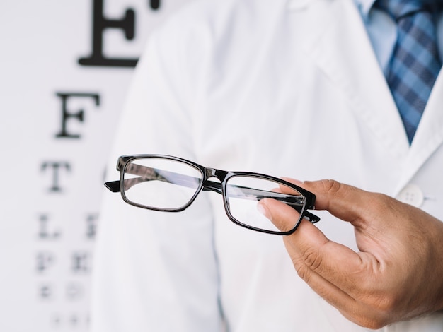 Männlicher Doktor, der ein Paar Brillen in seinen Händen hält