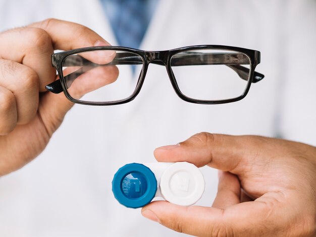 Männlicher Doktor, der Paar schwarze Gläser und Kontaktlinse zeigt