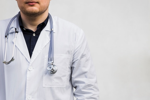 Männlicher Doktor mit Stethoskop um seinen Hals gegen weißen Hintergrund