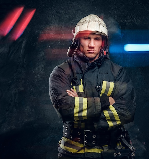 Männlicher Feuerwehrmann im Helm schaut im Studio auf schwarzem Hintergrund in die Kamera