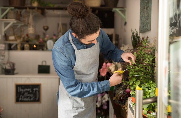 Männlicher Florist, der die Anlage im Blumenladen beschneidet