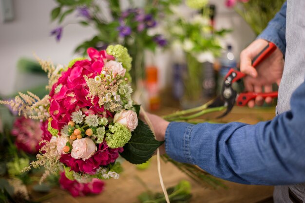 Männlicher Florist, der die bunten Blumenblumenstraußzweige mit Beschneidungsscheren schneidet