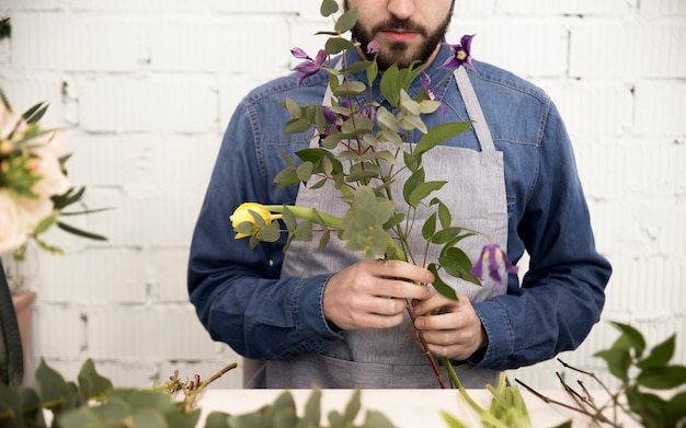 Männlicher Florist, der die Zweige und die Blume für die Herstellung des Blumenstraußes vereinbart