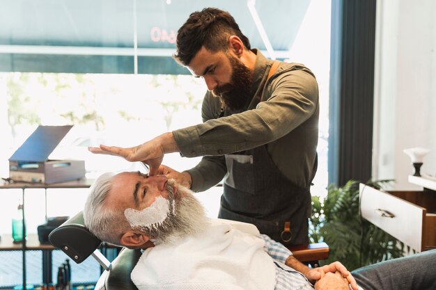 Männlicher Friseur, der für das Rasieren des älteren Kunden sich vorbereitet
