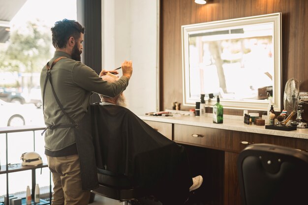 Männlicher Friseur, der Haar des älteren Kunden kämmt