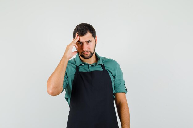 Männlicher Gärtner, der in denkender Pose in T-Shirt, Schürze steht und vernünftig aussieht, Vorderansicht.