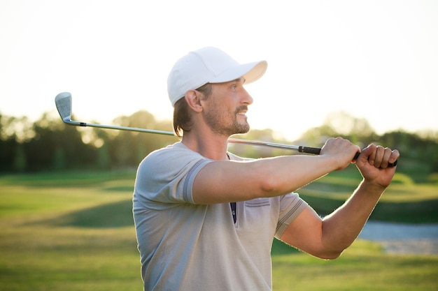 Männlicher Golfspieler lokalisiert auf schönem Sonnenuntergang Lächelnder Golfspieler mit weißem Hut auf dem Halten des Golfschlägers über Schulter