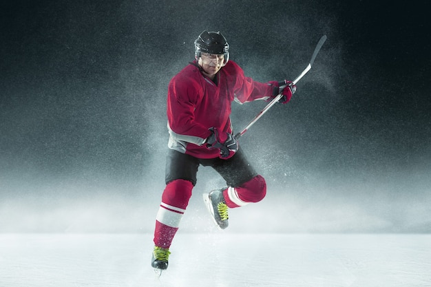 Kostenloses Foto männlicher hockeyspieler mit dem stock auf eisplatz und dunkler wand