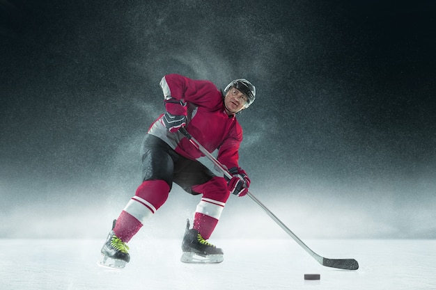 Kostenloses Foto männlicher hockeyspieler mit dem stock auf eisplatz und dunkler wand