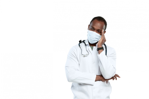 Männlicher junger Arzt mit Stethoskop und Gesichtsmaske lokalisiert auf Weiß