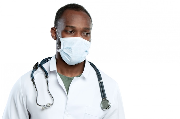 Männlicher junger Arzt mit Stethoskop und Gesichtsmaske lokalisiert auf Weiß