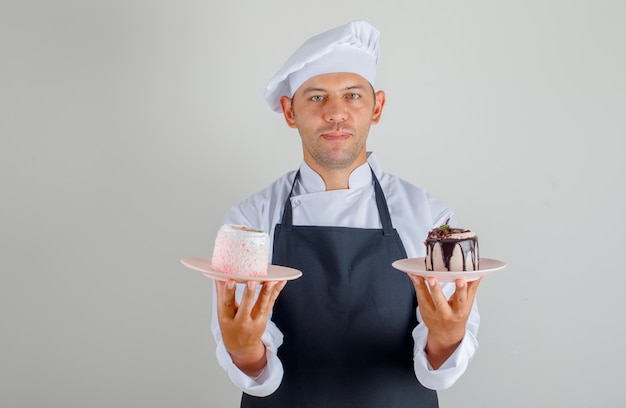 Kostenloses Foto männlicher koch, der dessertkuchen in tellern in hut, schürze und uniform hält