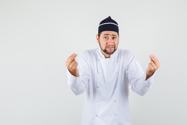 Männlicher Koch, der etwas in weißer Uniform erklärt und hilflos aussieht, Vorderansicht.