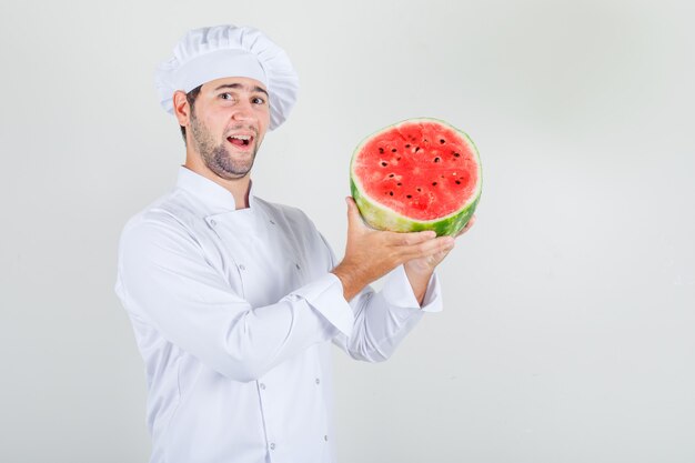 Männlicher Koch, der geschnittene Wassermelone in der weißen Uniform hält und glücklich schaut.