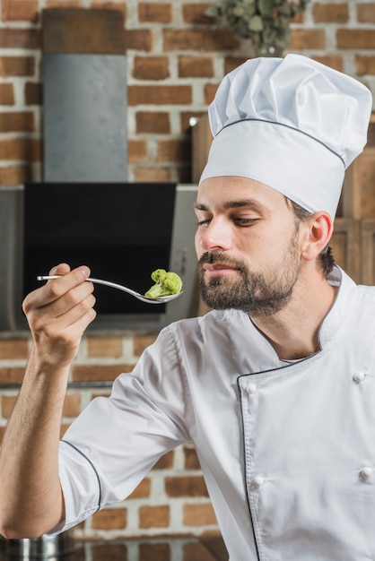 Männlicher koch, der grünen brokkoli im löffel riecht