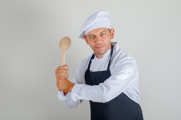 Männlicher Koch, der Holzlöffel im Hut, in der Schürze und in der Uniform hält