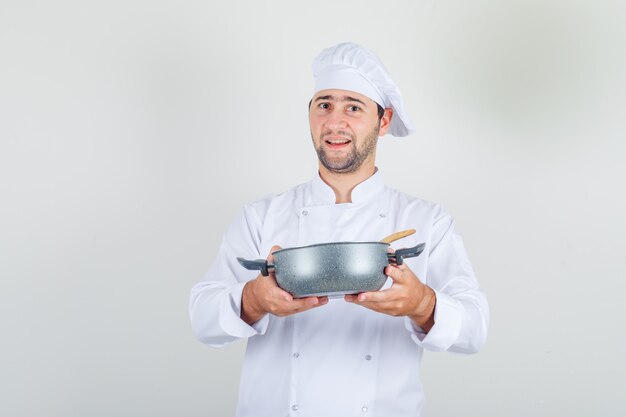 Männlicher Koch, der Suppe im Topf in der weißen Uniform hält und glücklich schaut