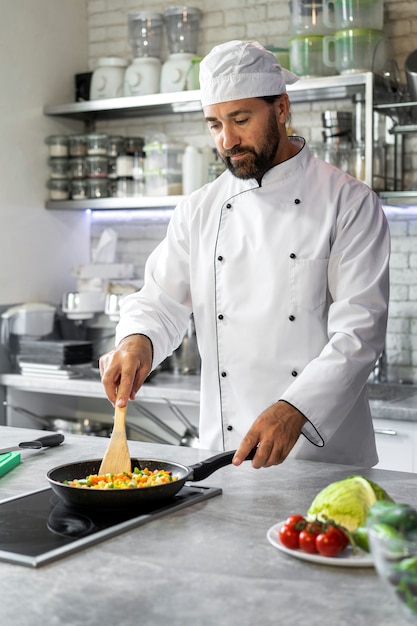 Männlicher Koch in der Küche, der Teller in einer Bratpfanne kocht