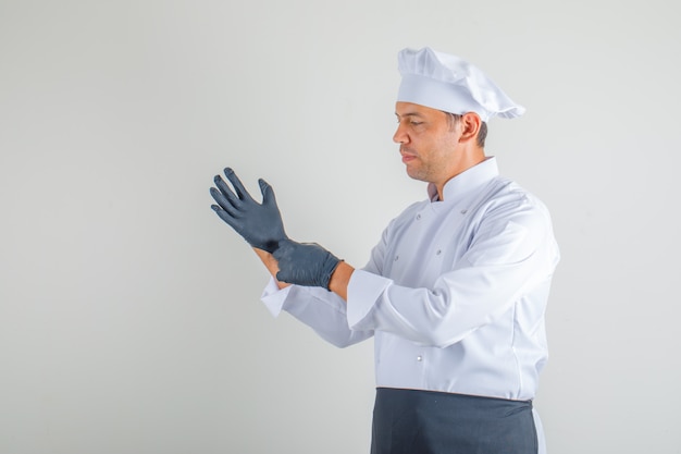 Männlicher Koch in Uniform, Schürze und Hut, die Handschuhe tragen und vorsichtig schauen