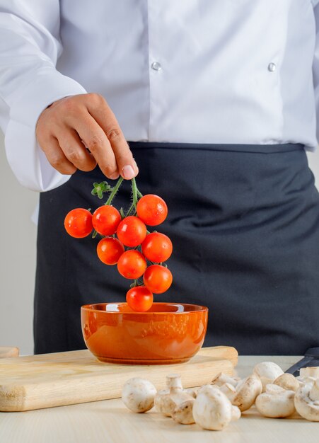 Männlicher Koch in Uniform und Schürze, die Tomaten aus der Schüssel in der Küche nehmen