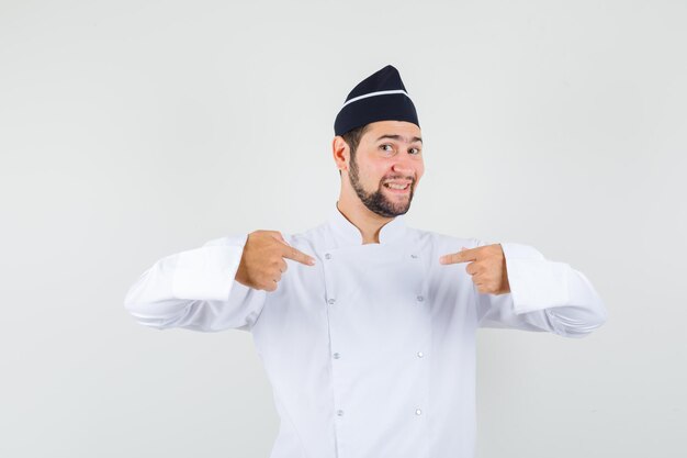 Männlicher Koch in weißer Uniform, der auf sich selbst zeigt und stolz aussieht, Vorderansicht.