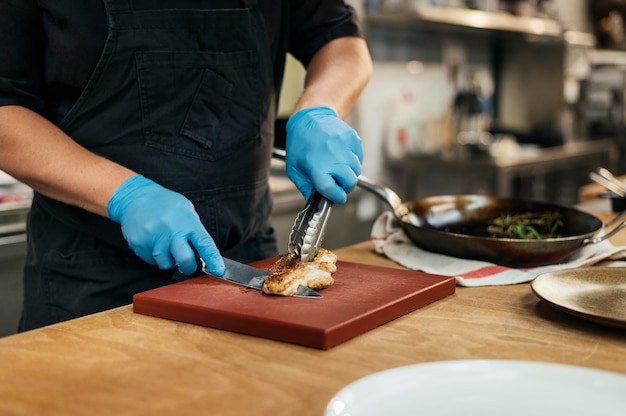 Männlicher Koch mit Handschuhen, die Fleisch hacken