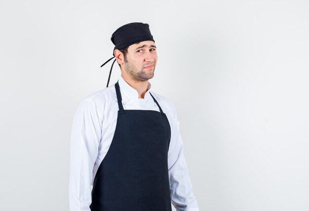 Männlicher Koch mit stirnrunzelndem Gesicht in Uniform, Schürze und unzufrieden aussehend, Vorderansicht.