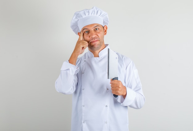 Männlicher Kochkoch hält Messer für Fleisch und denkt in Uniform und Hut und sieht positiv aus