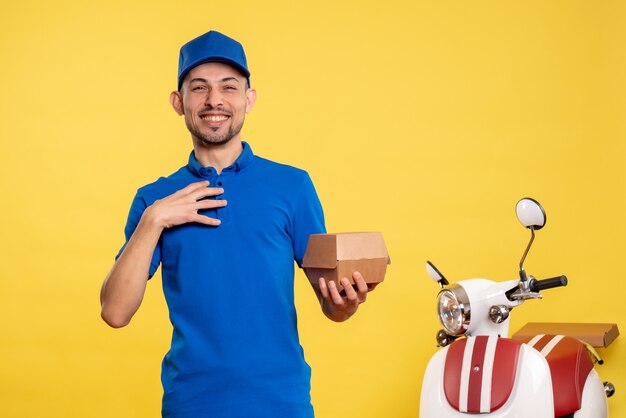 Männlicher Kurier der Vorderansicht, der kleines Lebensmittelpaket auf gelber Arbeitsdienstuniform-Fahrradarbeitslieferung hält