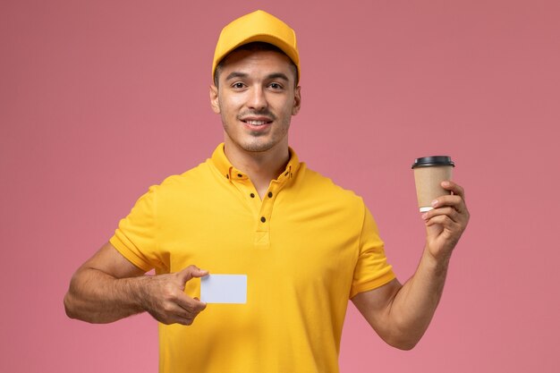 Männlicher Kurier der Vorderansicht in der gelben Uniform, die die Kaffeetasse und die Karte der Lieferung auf rosa Hintergrund hält