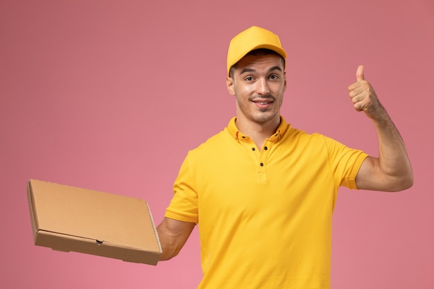 Männlicher kurier der vorderansicht in der gelben uniform, die lebensmittelabgabebox auf dem rosa hintergrund hält