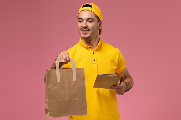 Männlicher Kurier der Vorderansicht in der gelben Uniform, die Liefernahrungsmittelpaket auf dem rosa Hintergrund hält.
