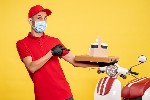 Männlicher Kurier der Vorderansicht in der Maske mit Lieferkaffee und -schachtel auf der Arbeitsuniform des gelben Service covid pandemic color virus